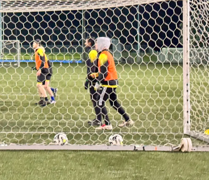 Footballers training under floodlights at night, seen through the goal net